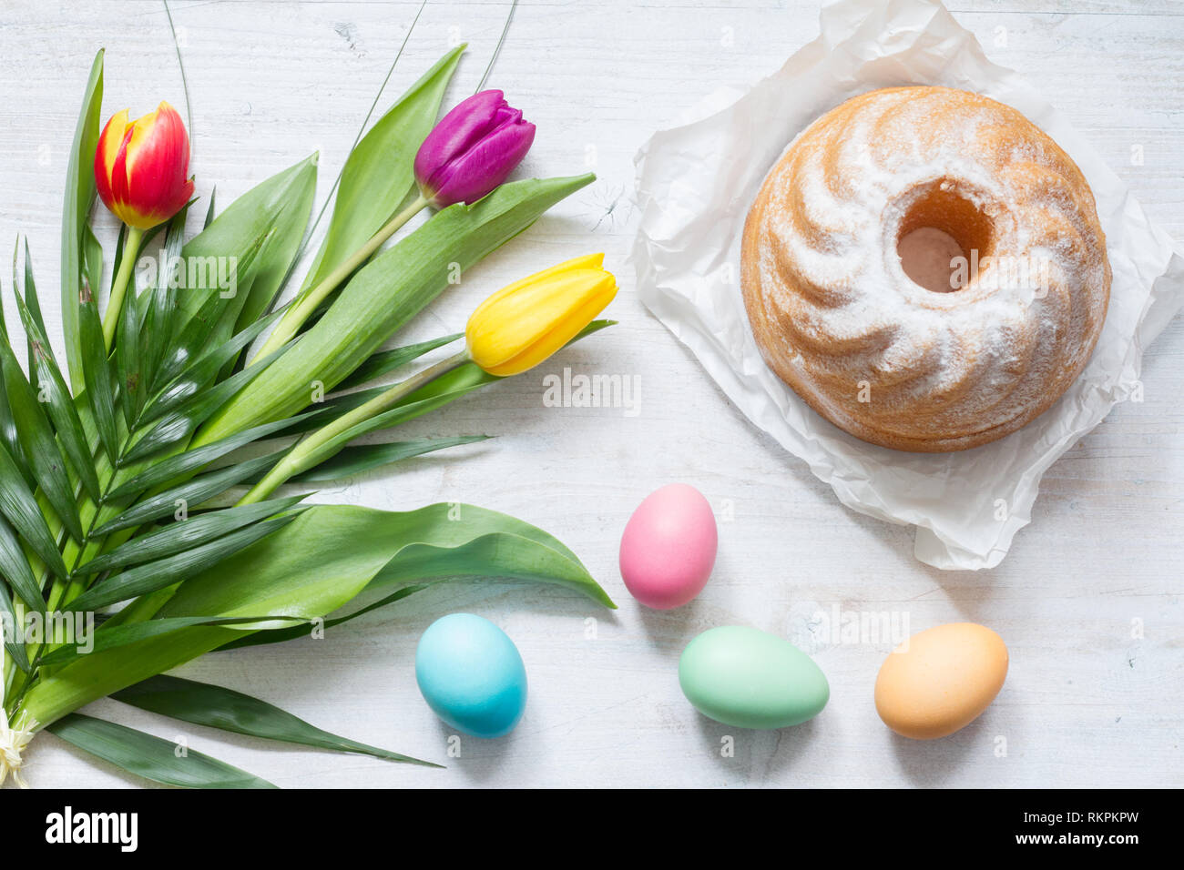 Ostern bunte Frühling Tulpen mit Palm cross Kuchen und Eier Dekoration auf weißem Holz- natürlichen Hintergrund Stockfoto