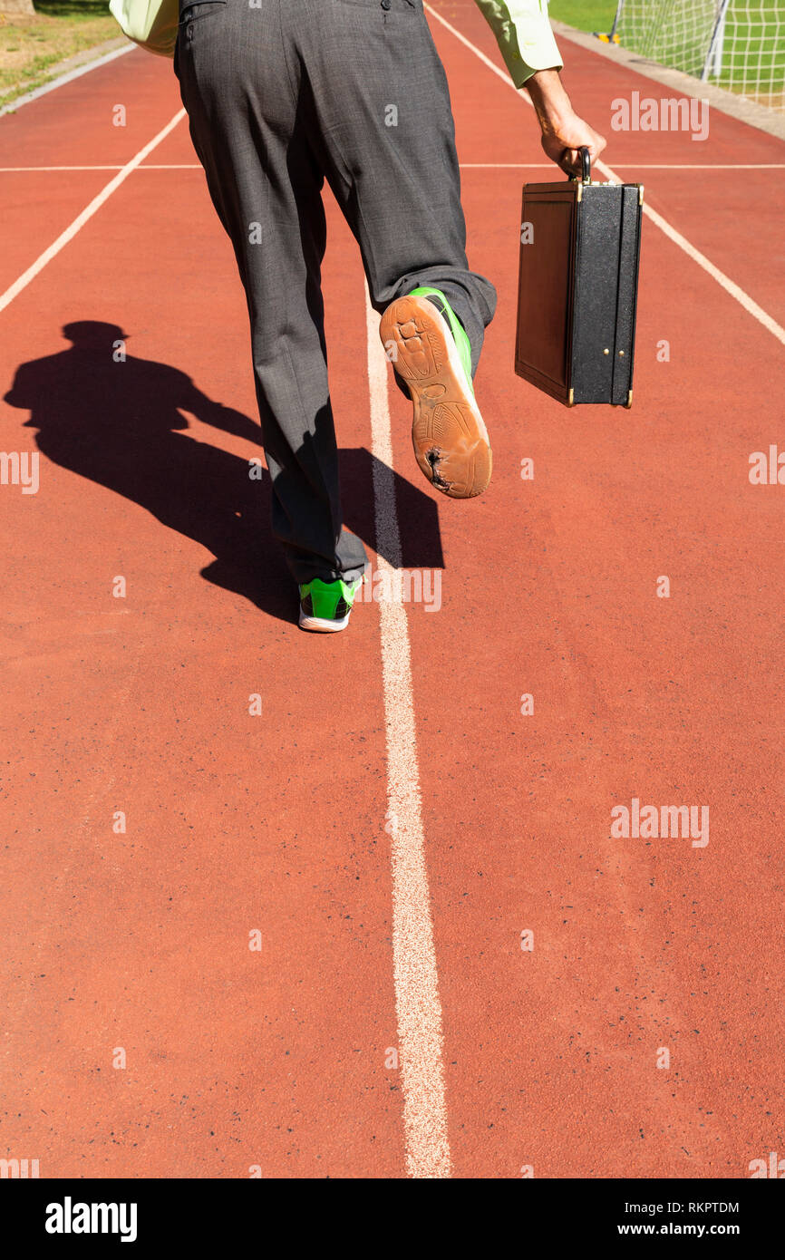 Ein Mann im grauen Anzug mit grünem Hemd, schwarze Aktentasche und Kabelbruch im grünen Sport Schuhe laufen auf eine Laufstrecke. Stockfoto