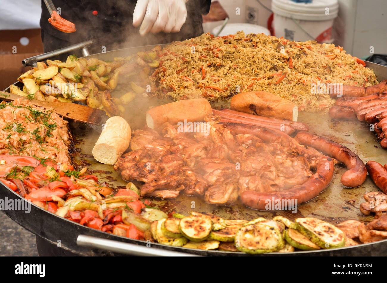 Zersetzt Street Food auf einer großen Wanne aus Metall, aus der Nähe. Fried Chicken, Würstchen, gebratenen Zucchini, Fleisch, Fisch, usbekischer Pilaw, gebratenen Kartoffeln und Weißbrot. Stockfoto