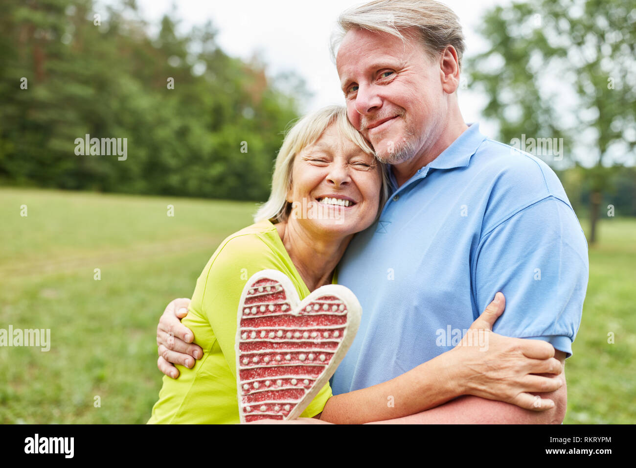 Ältere Frau umarmen in der Liebe Ihr Partner mit einem Lebkuchen Herz in den Händen Stockfoto