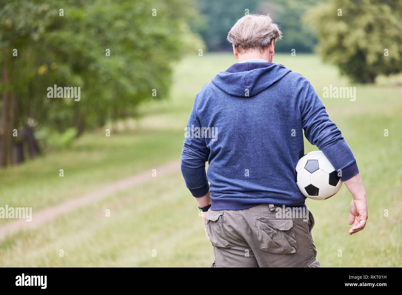 Älterer Mann mit einem Fußball unter dem Arm auf einer Wiese im Park Stockfoto