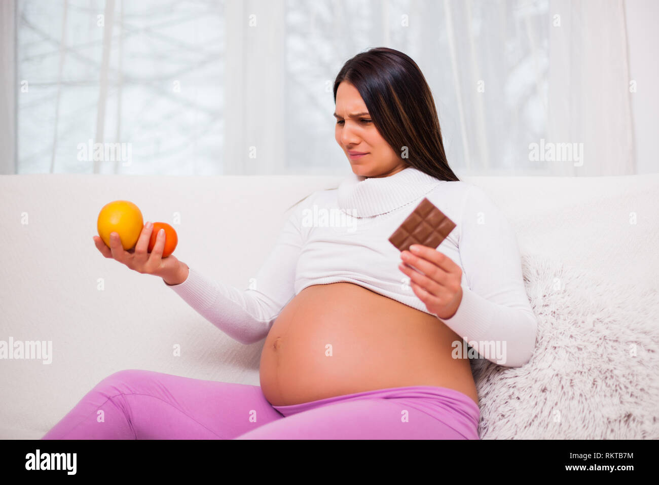 Schwangere Frau ist die Entscheidung candy von frischem Obst zu essen. Stockfoto