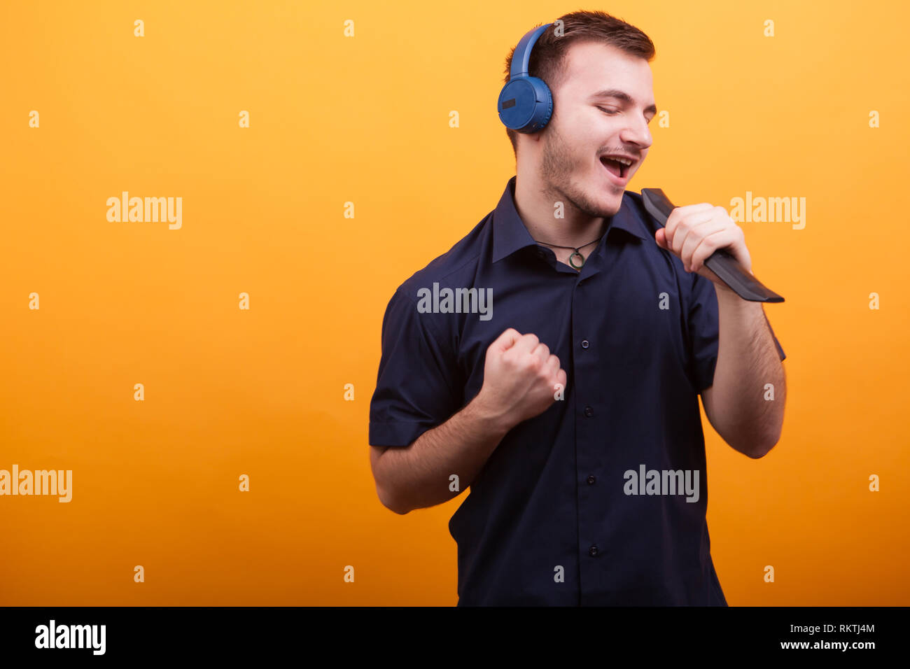 Junger Mann singen amd gut fühlen, während Sie die Kopfhörer auf gelben Hintergrund. Großartige Musik. Stockfoto