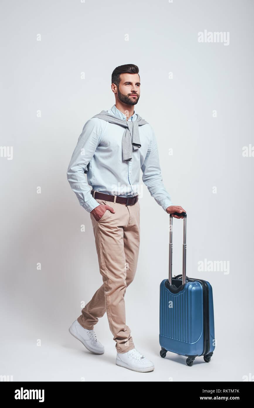 Travel Concept. Volle Länge des charmanten bärtiger Mann mit einem Gepäck beim Stehen auf einem grauen Hintergrund. Studio shot Stockfoto