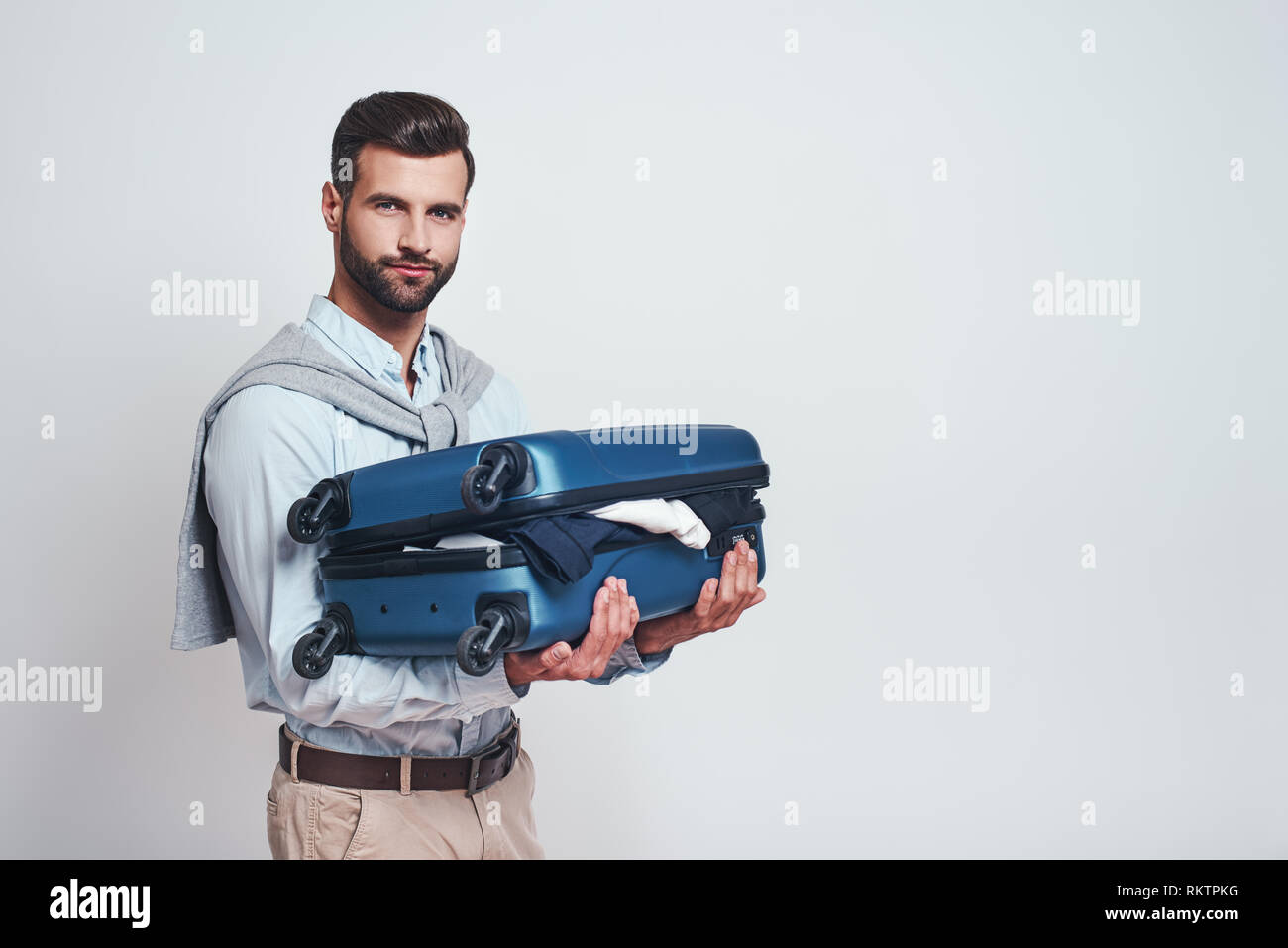 Ich komme wieder. Positive und stattlicher Mann mit Koffer und bereit zu reisen. Travel Concept. Grauer Hintergrund Stockfoto