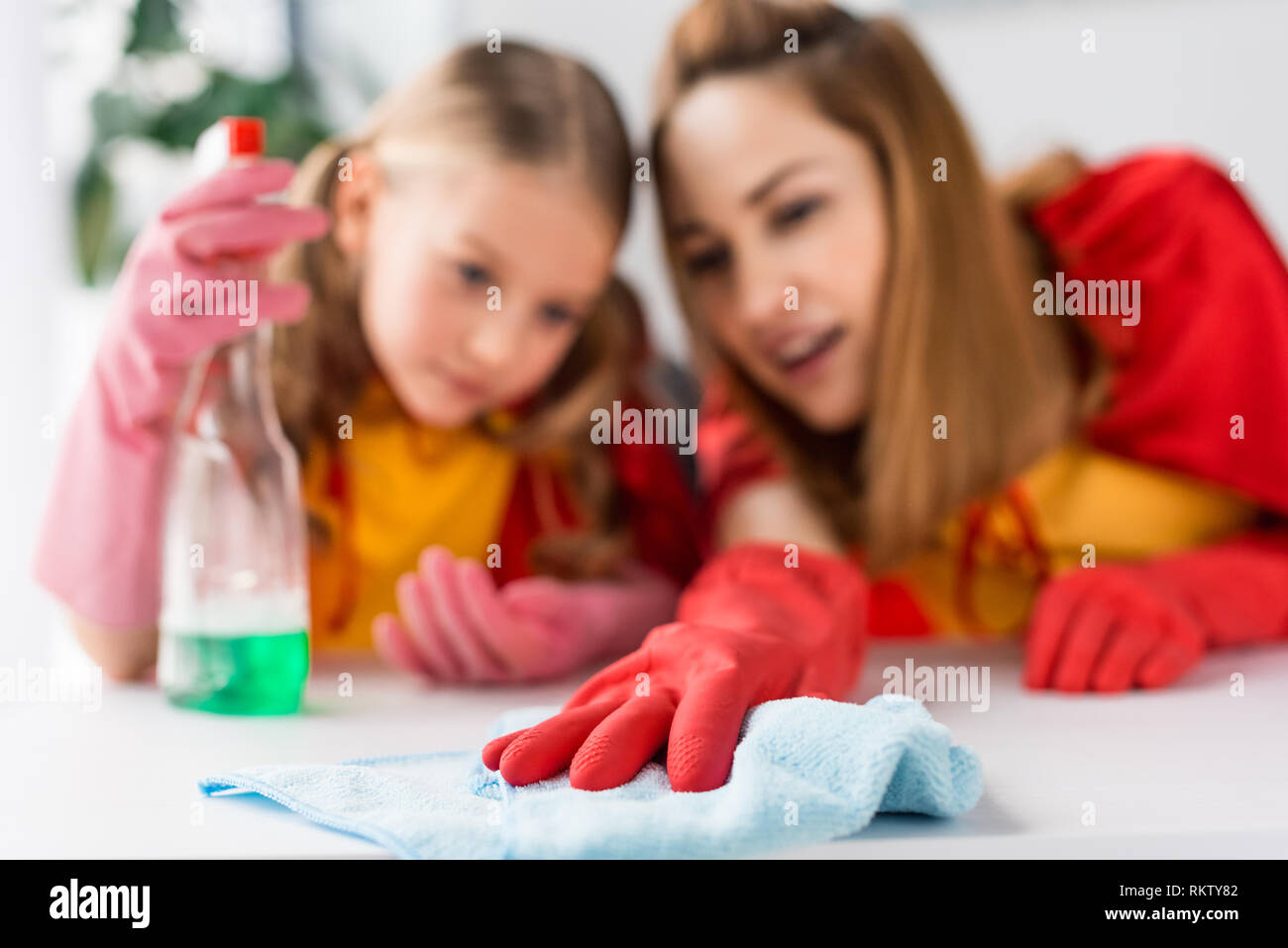 Selektiver Fokus von Mutter und Tochter in Red Caps und Gummihandschuhe abstauben zu Hause Stockfoto