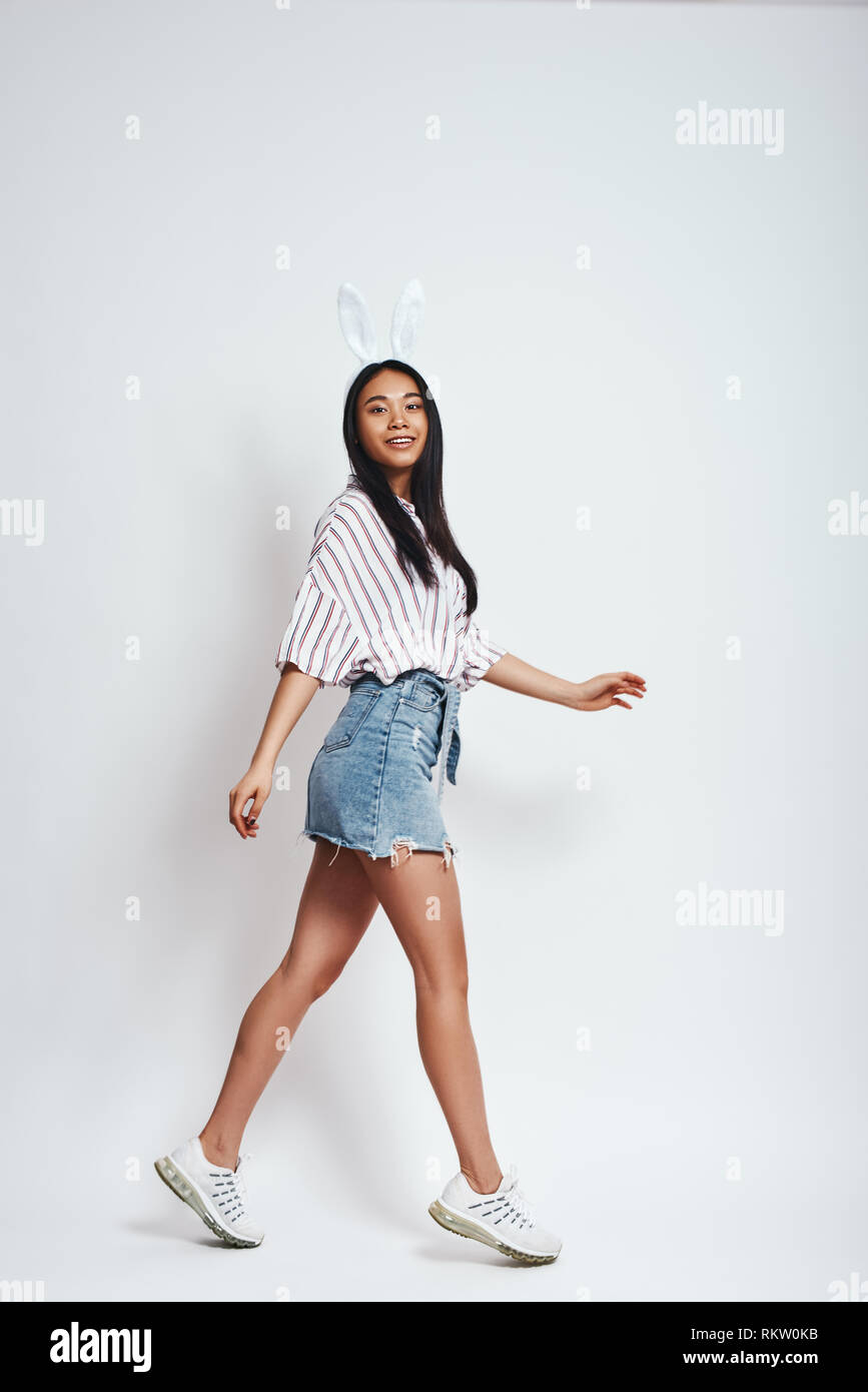 Sorglos und glücklich. Volle Länge des lächelnden jungen asiatischen Frau in Hasenohren und Freizeitbekleidung auf grauem Hintergrund. Glück Konzept Stockfoto