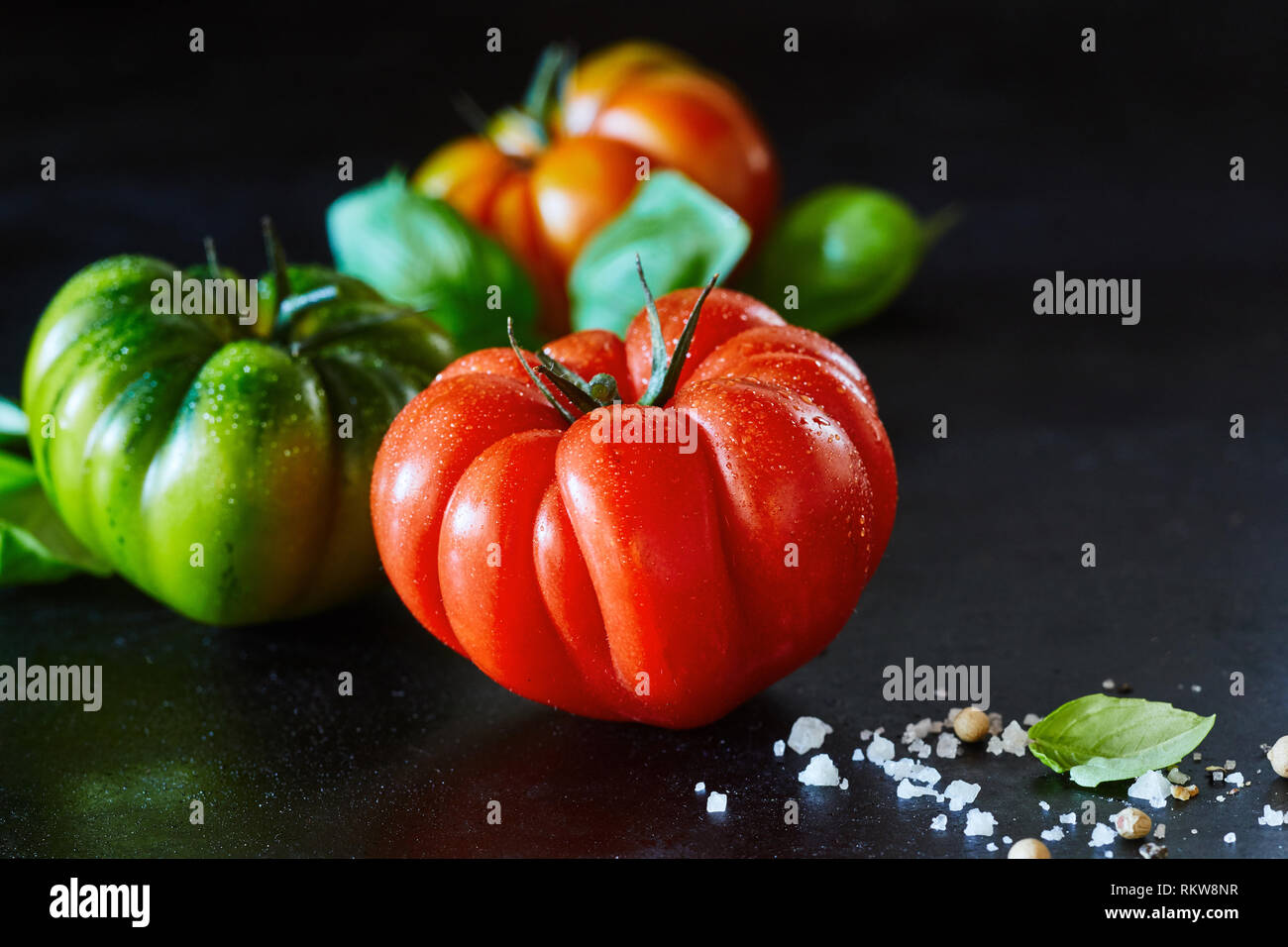 Gesund ganze Nasse frische reife rote Tomaten mit Wassertropfen und Gewürze auf einem schwarzen reflektierenden Hintergrund mit Kopie Raum und zwei zusätzliche Tomaten Stockfoto