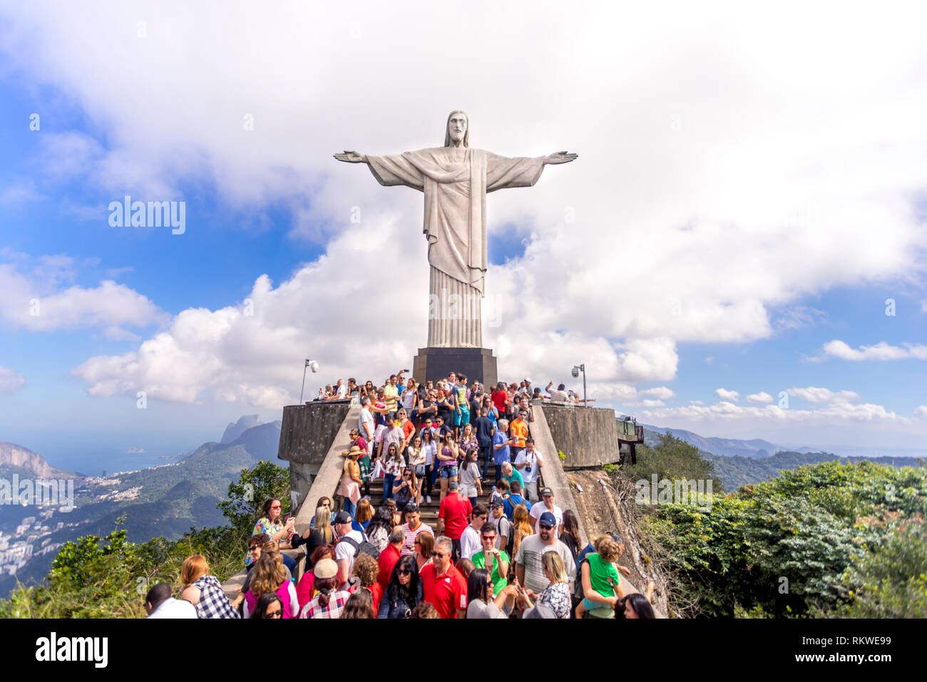 Klare Sicht auf eine Masse von Touristen oben auf dem Berg Corcovado in Rio de Janeiro mit der Christusstatue Hoch über Ihnen und einer Wolke hinter Stockfoto