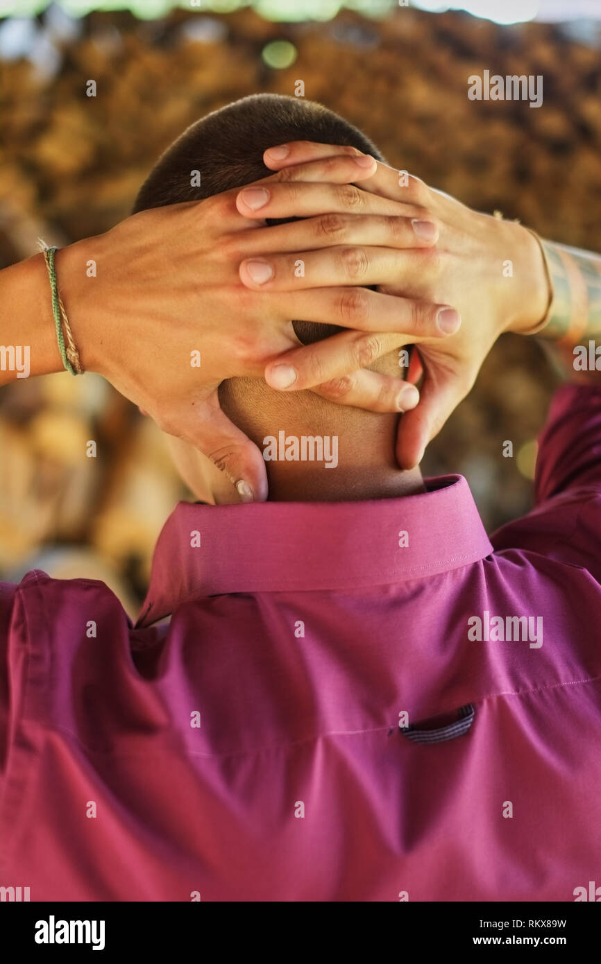 Junger Mann von der Rückseite, steht mit die Arme hinter dem Kopf gefaltet, Hände in die Burg, sieht am Horizont Stockfoto