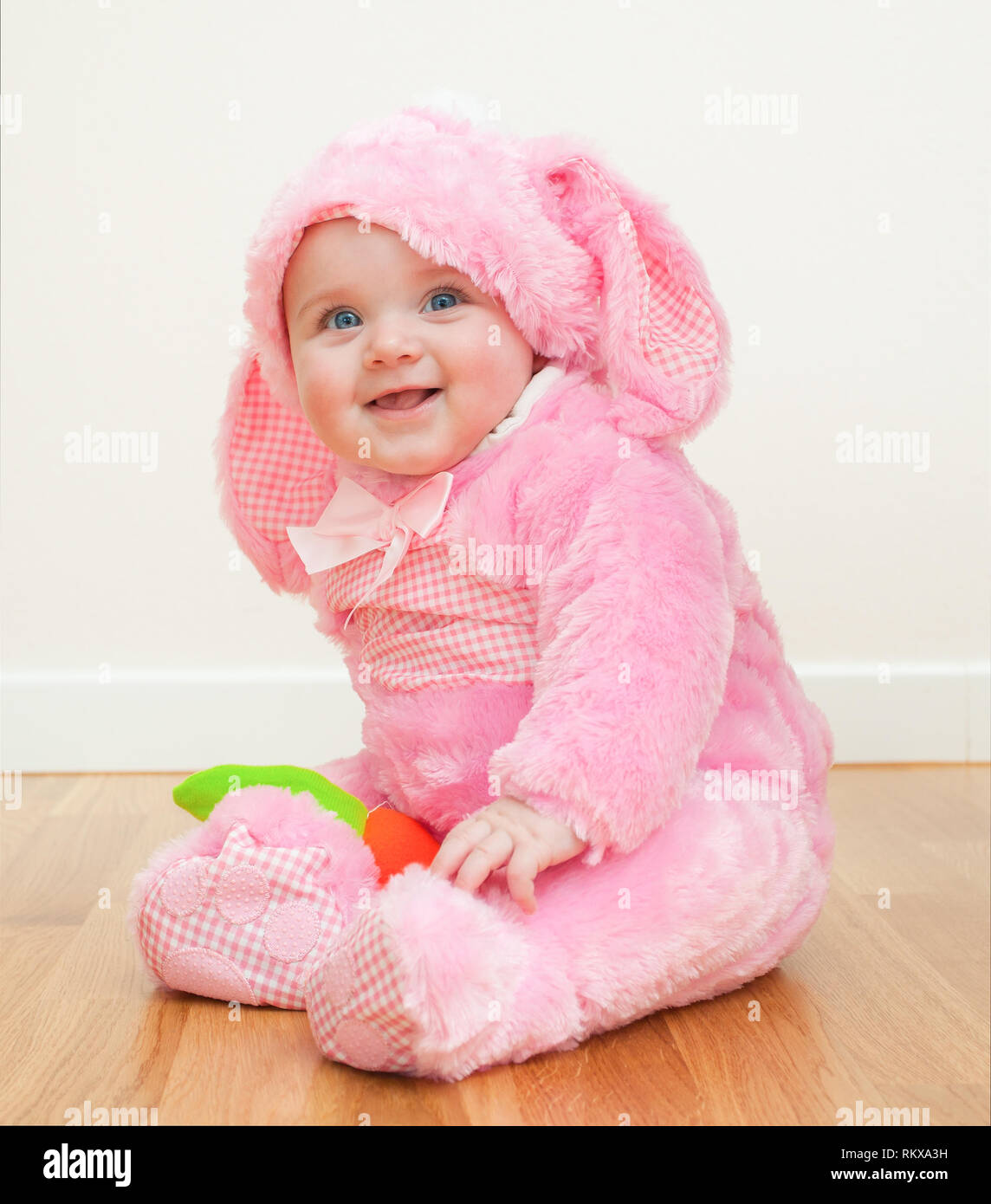 Kleinen niedlichen Baby in einem rosa Bunny Suit. Sitzt das Kind auf dem Holzboden. Stockfoto