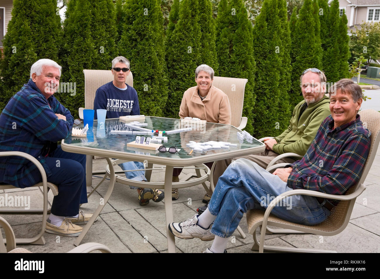 Erwachsene Domino spielen; Spiel, Schiefer im Außenbereich; Terrasse; Freunde; Spaß; Freundschaft; immergrüner Baum Privacy Screen; Herbst; Horizontal; HERR, P Stockfoto