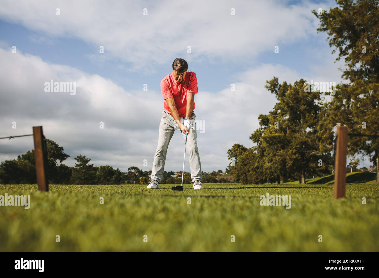 Low Angle Shot männlicher Golfspieler nehmen Schuß stehend auf dem Feld. Volle Länge des älteren Golf Player über den Schuß zu nehmen. Stockfoto