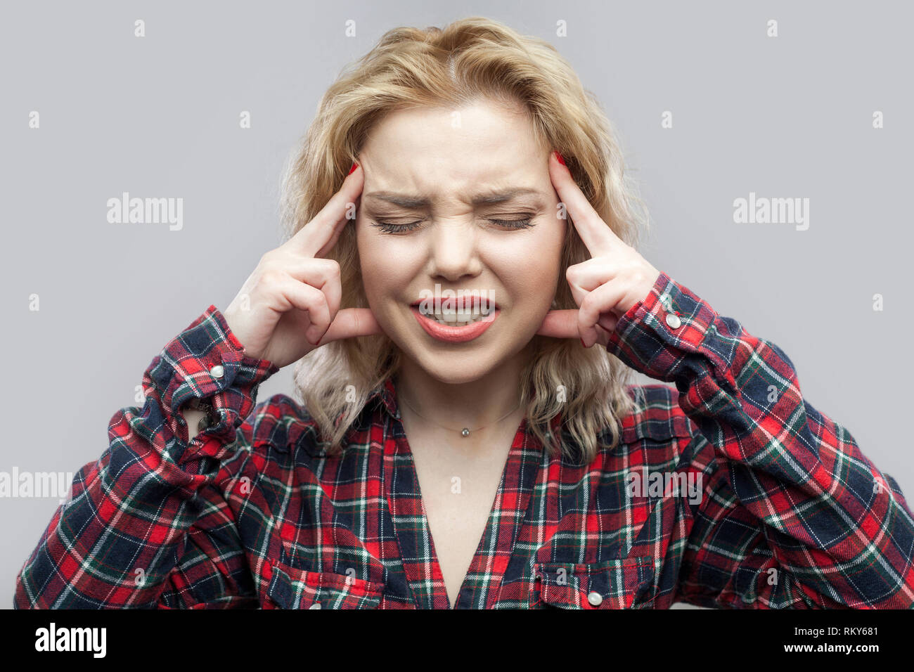 Kopfschmerzen oder Verwirrung. Portrait von verwirrt oder krank blonde Frau im casual rot kariertem Hemd stehen, berühren, Tempel, geschlossenen Augen und ballte te Stockfoto