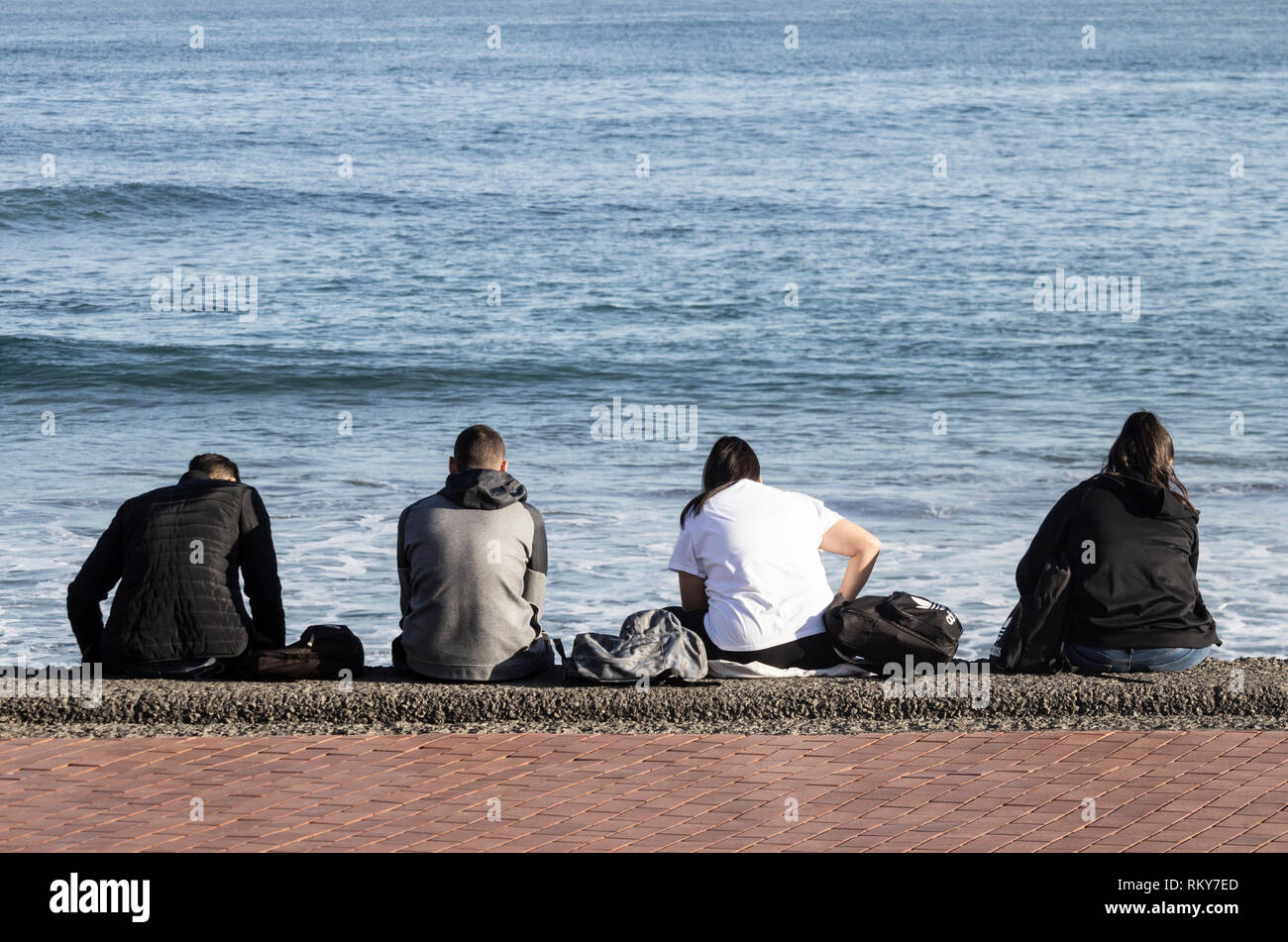 Ansicht der Rückseite vier Teenager sitzen auf Sea Wall und Handys: Langeweile, gelangweilte Teenager, Social Media... Konzept. Stockfoto