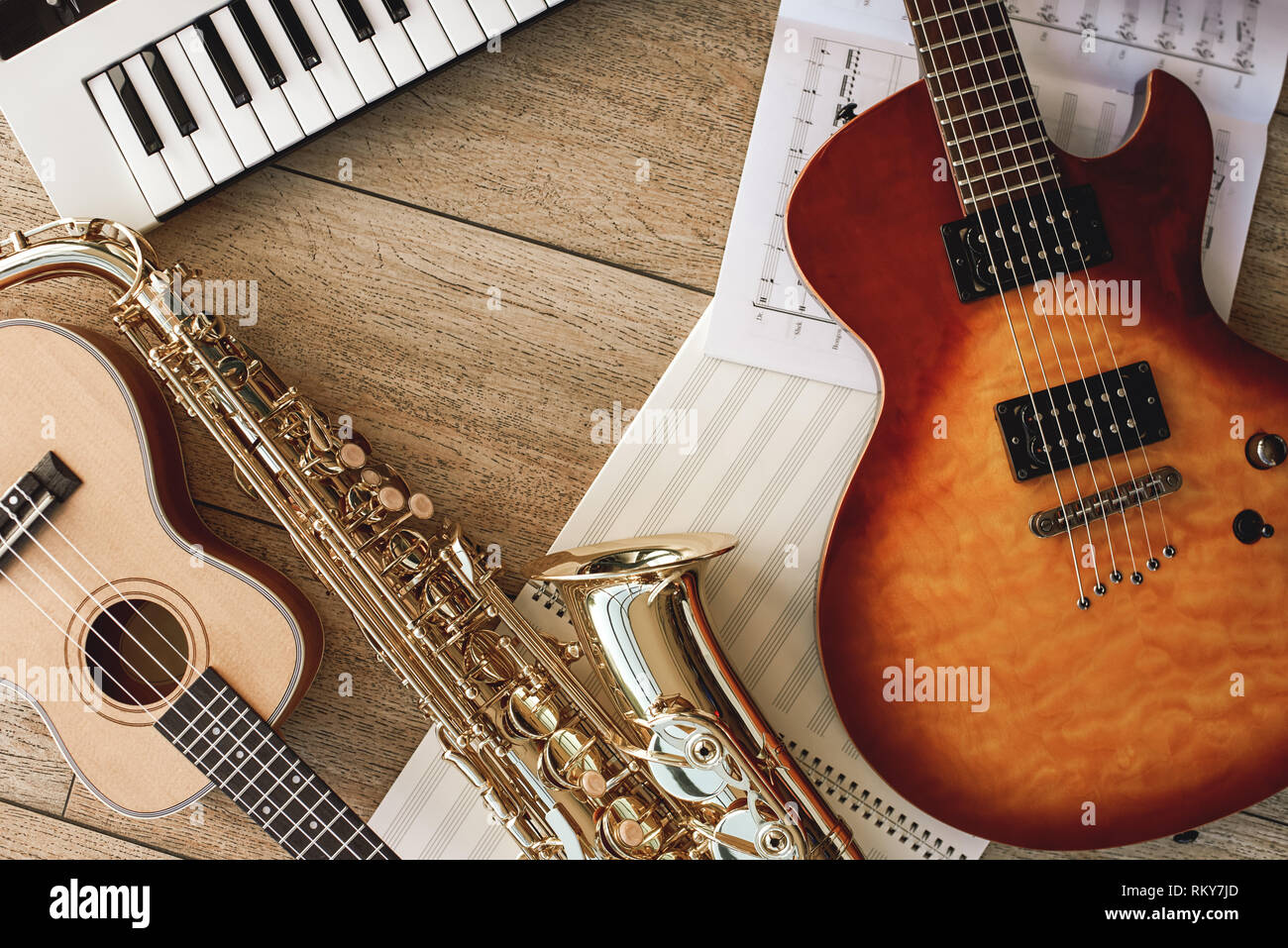 Zusammensetzung der verschiedenen Musikinstrumente: Synthesizer, E-Gitarre,  Saxophon und Ukulele liegen, Blätter mit Noten liegen auf Holzboden und.  Musikinstrumente. Musik Equipment Stockfotografie - Alamy