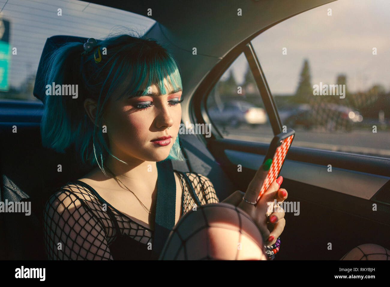 Junges Mädchen mit blauen Haaren Reiten im Auto mit Handy. Stockfoto