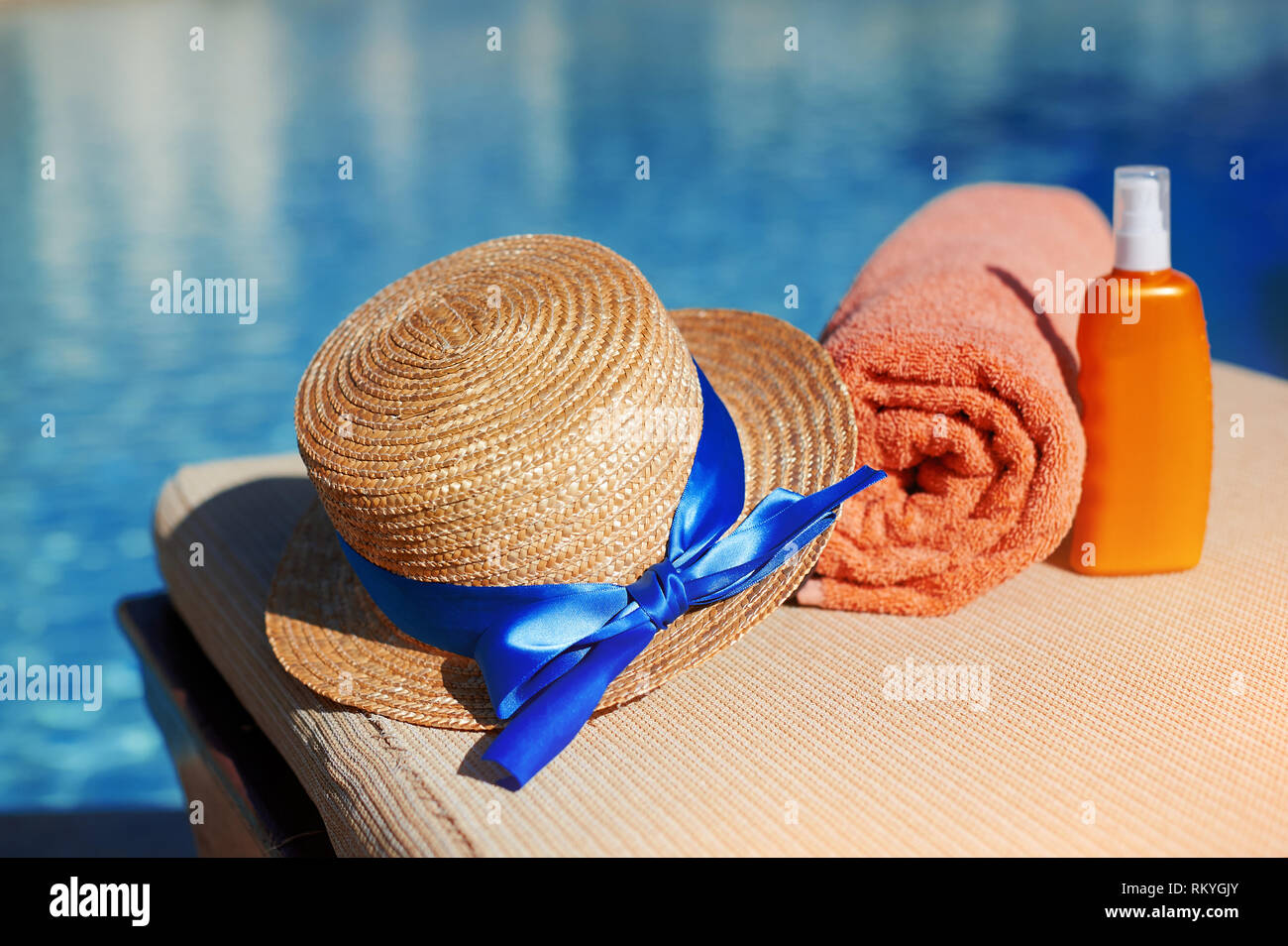 Orange Baumwolle Handtuch und Sonnencreme Bodylotion und Hut in einem orange Rohr auf dem Hintergrund Pool. Mittel für die Hautpflege, Konzept Sommer Entspannung und Stockfoto