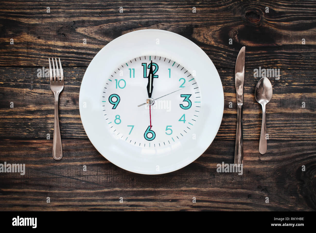 Zwölf Stunden intermittierender Fasten zeit Konzept mit Uhr auf Platte über einen rustikalen Holztisch/Hintergrund. Ansicht von oben. Stockfoto