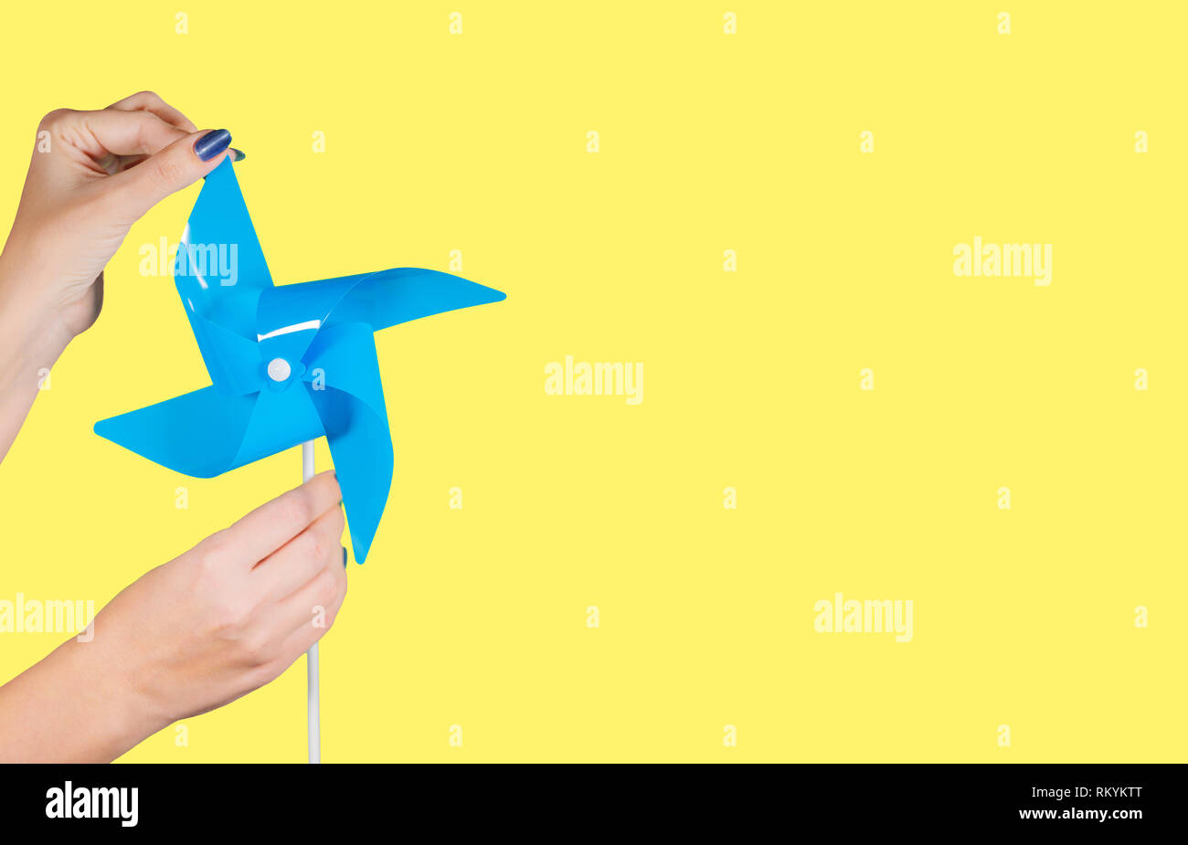 Detailansicht der weiblichen Händen mit blauen Maniküre holding Blue pinwheel isoliert auf gelben Hintergrund mit Copyspace. Horizontale Farbfoto Stockfoto