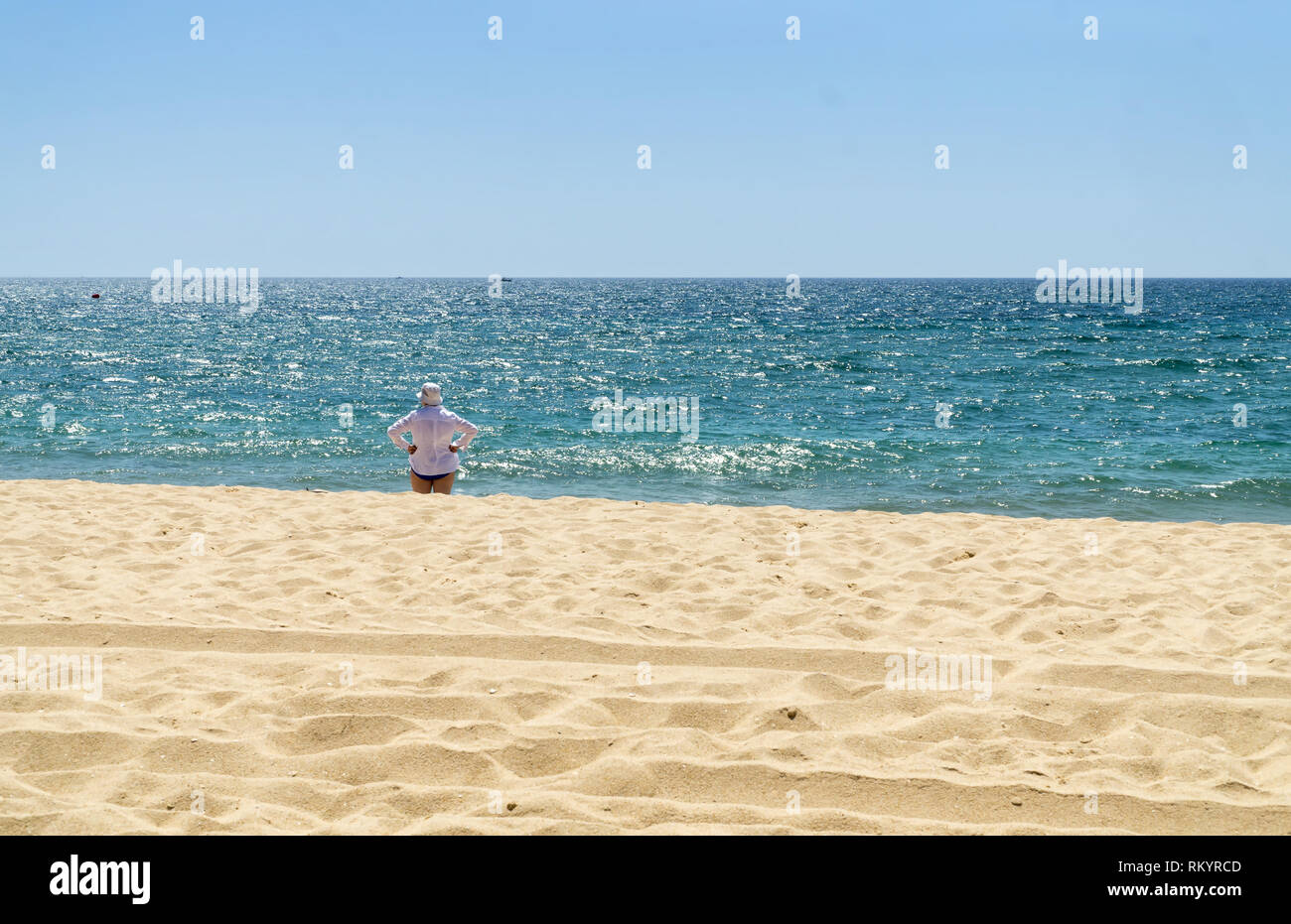 Reife Frau in weißem Hemd und weißen Hut steht auf den Strand und das Meer im sonnigen Sommertag. Stockfoto