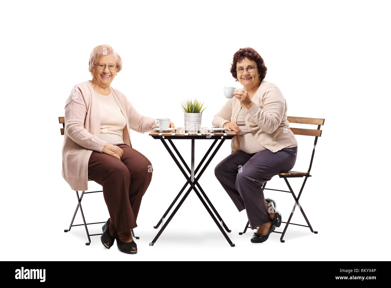 In voller Länge Porträt von zwei älteren Frauen sitzen an einem Tisch, trinkt Kaffee und lächelnd in die Kamera auf weißem Hintergrund Stockfoto