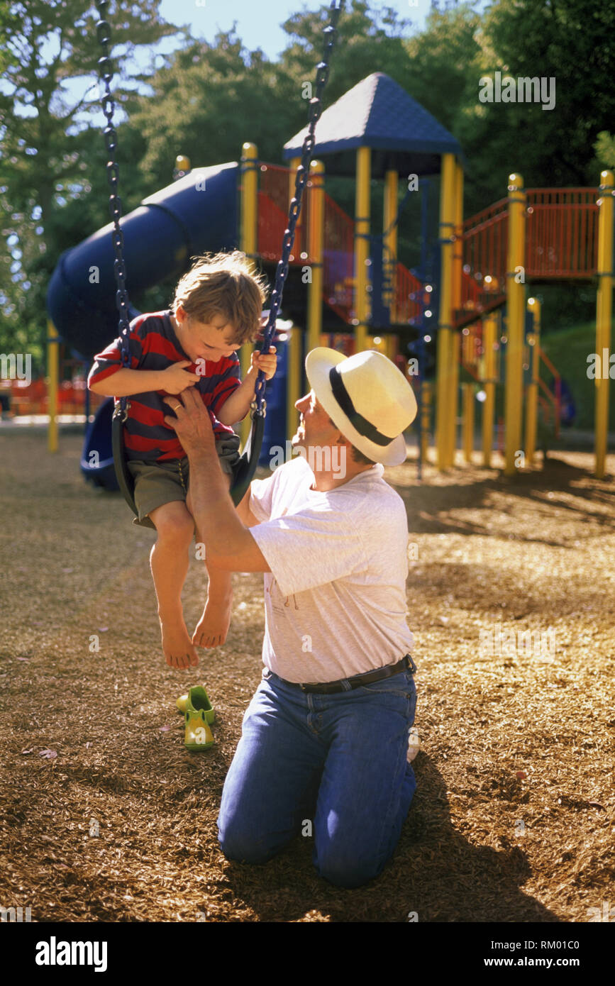 Ein Sohn von seinem Vater gekitzelt werden, während auf einer Schaukel im Park. Stockfoto