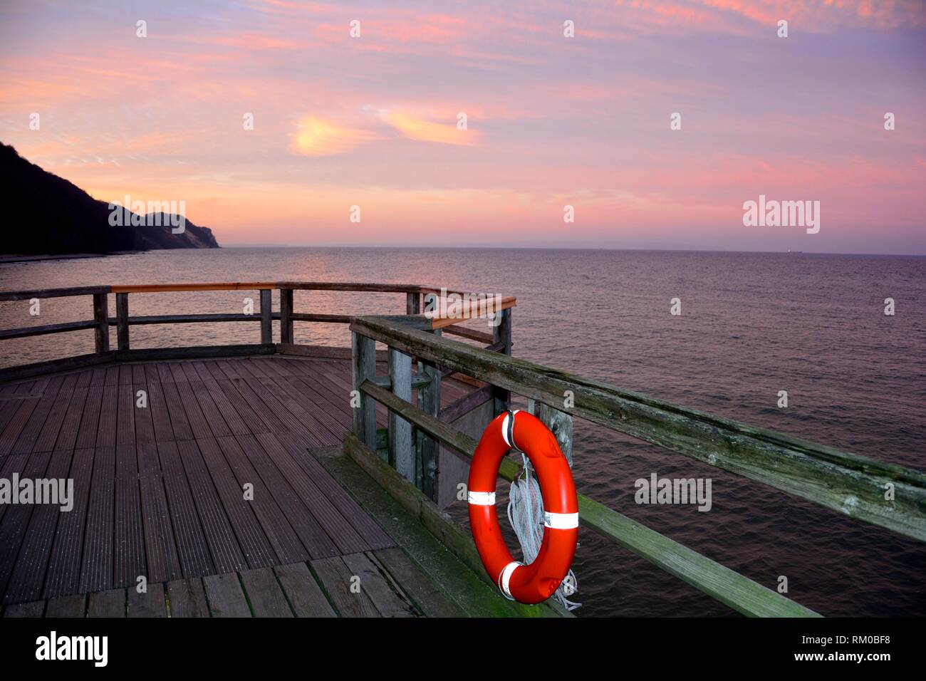 Hölzerne Seebrücke mit einem roten Rettungsring an der Ostsee nach Sonnenuntergang mit Blick auf das Meer mit Kopie Raum Stockfoto