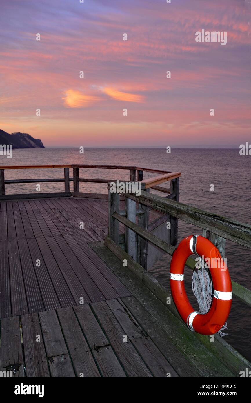 Hölzerne Seebrücke mit einem roten Rettungsring an der Ostsee nach Sonnenuntergang mit Blick auf das Meer mit Kopie Raum Stockfoto