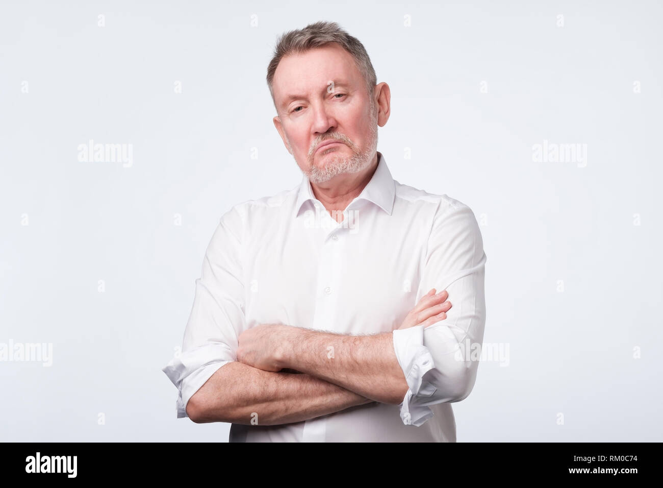 Älterer Mann im weißen Hemd mit verschränkten Armen auf der Suche gedrückt und genervt Stockfoto