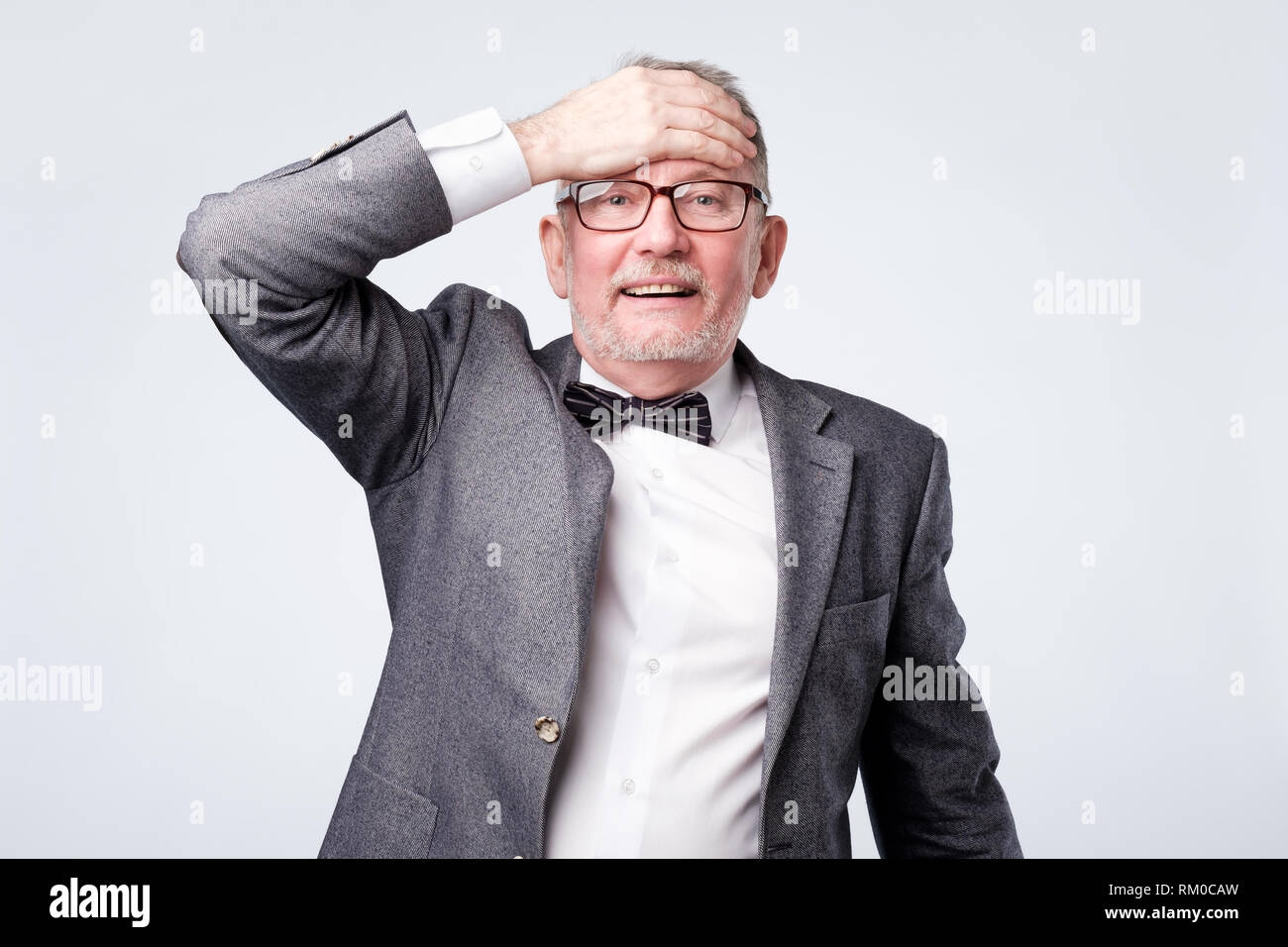 Älterer Mann im Anzug mit Fliege mit der Hand überrascht auf dem Kopf für Fehler Stockfoto