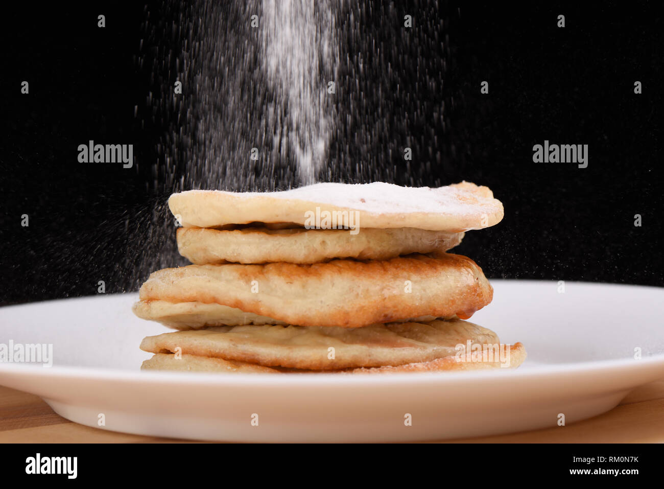 Haferflocken bestreuen Pfannkuchen mit Puderzucker. Weiße Platte auf einem hölzernen Hintergrund Stockfoto