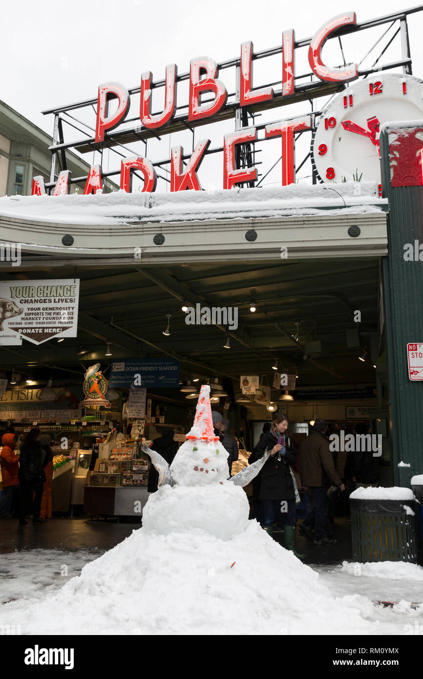 Seattle, Washington: ein Schneemann mit Waffen von gefrorenem Lachs sitzt vor dem Wahrzeichen der Pike Place Fish Market als starker Wintersturm decken die c Stockfoto