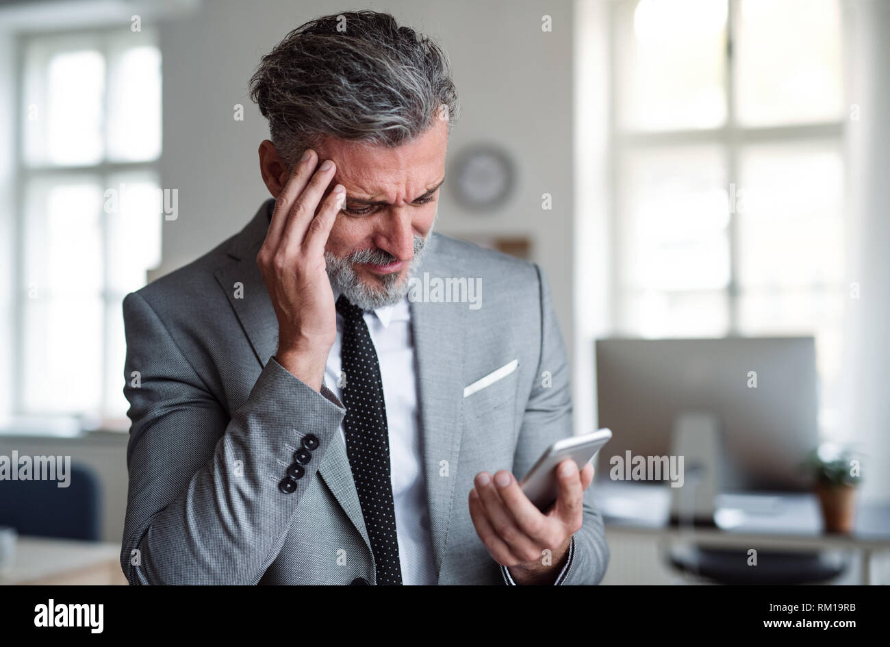 Ein frustrierter Geschäftsmann mit Smartphone steht in einem Büro, lesen schlechte Nachrichten. Stockfoto