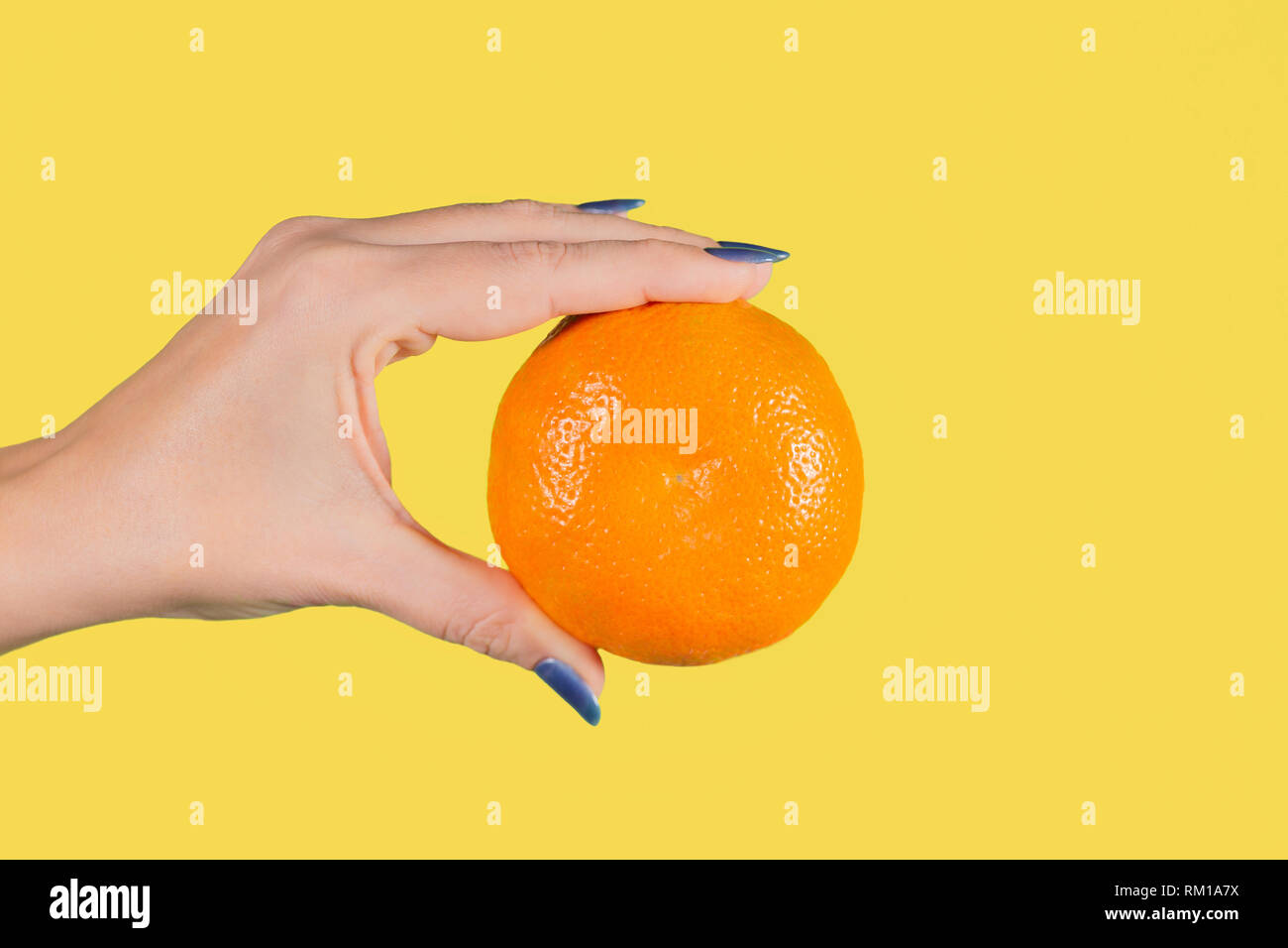 Detailansicht schöne weibliche Hand, die grosse Orange reif Mandarin auf gelbem Hintergrund. Gesunde Ernährung Konzept. Horizontale Farbe Hg Stockfoto