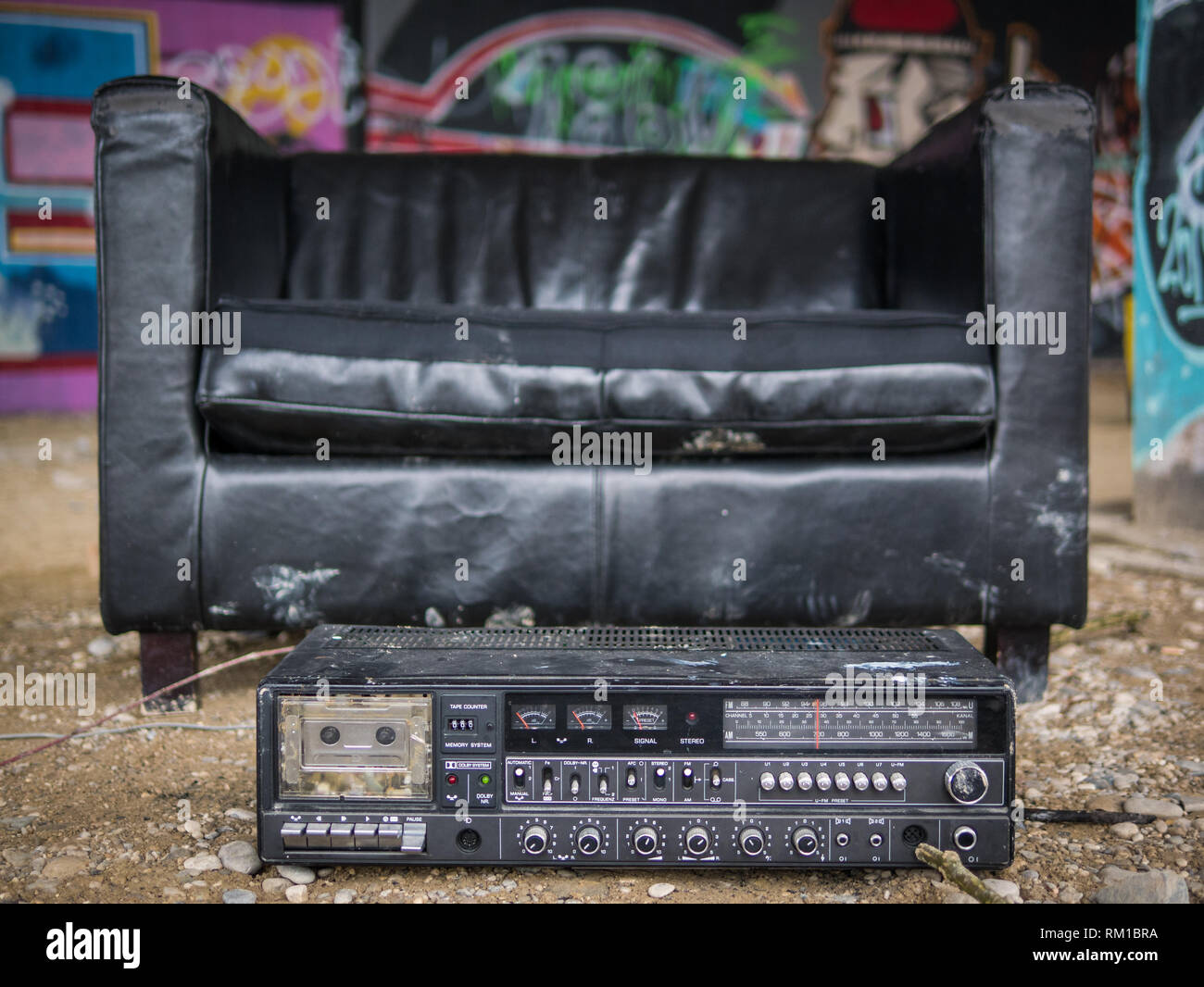 Schwarze Ledersessel und altes Radio in einem gekühlten kreative Schutz unter einer Brücke mit Graffitis im Hintergrund Stockfoto