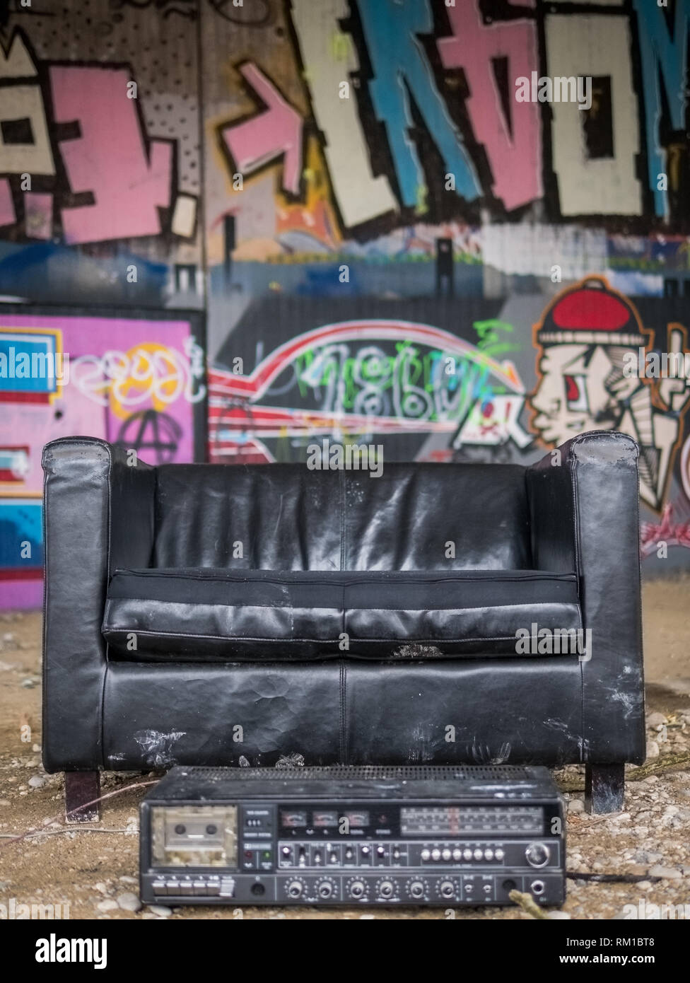 Schwarze Ledersessel und altes Radio in einem gekühlten kreative Schutz unter einer Brücke mit Graffitis im Hintergrund Stockfoto