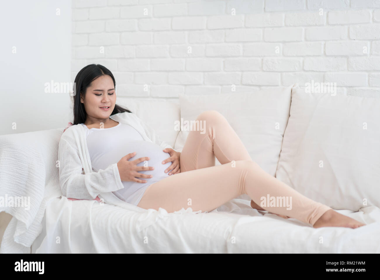 Jungen Asiatischen schwanger sitzen im Wohnzimmer und haben einige wehen. Stockfoto