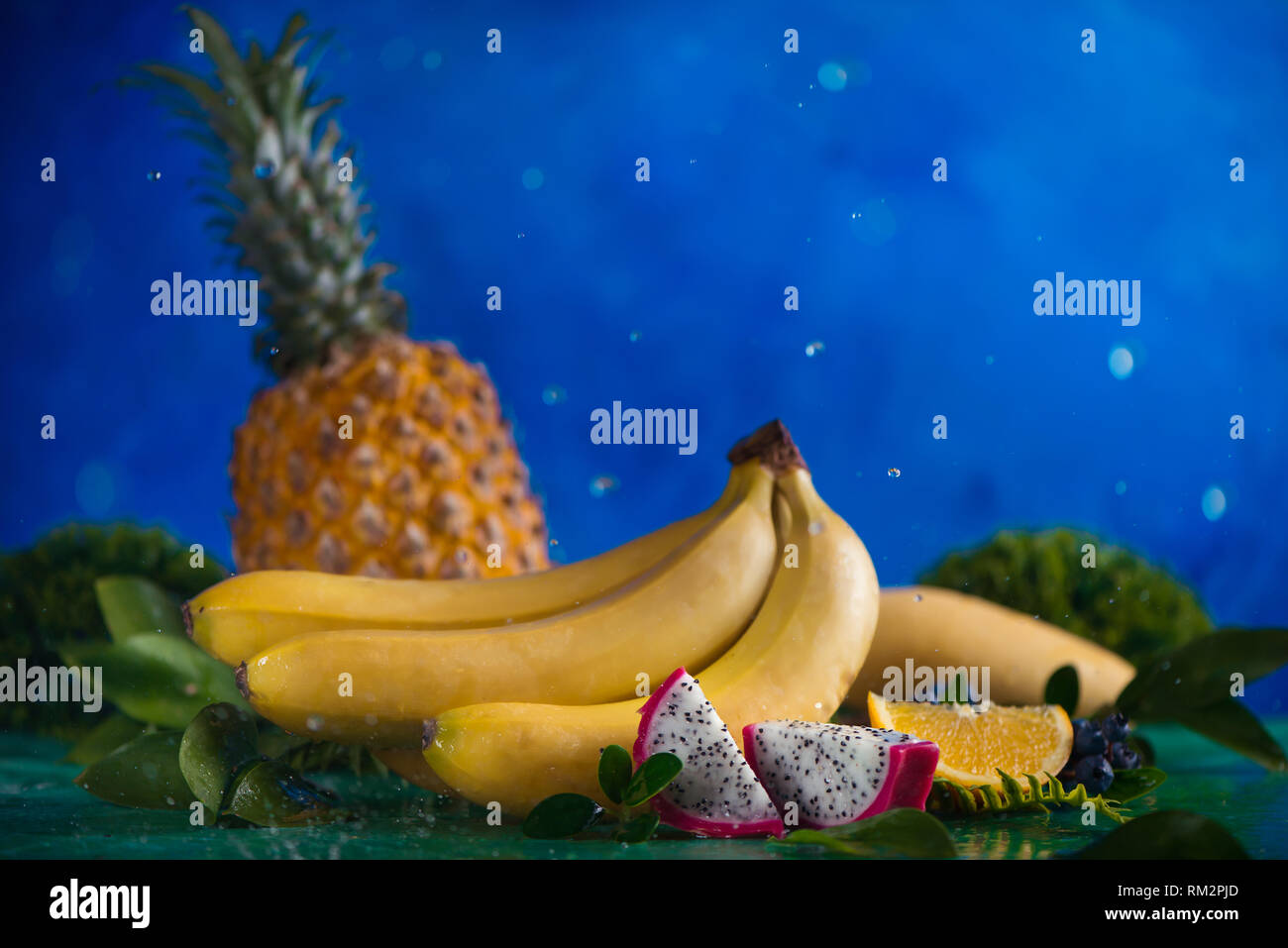 Ananas, Bananen, Mango, Drachenfrucht mit tropischen Blätter auf einem blauen Hintergrund mit Wassertropfen und Platz kopieren Stockfoto