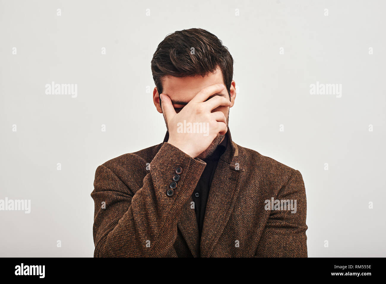 Porträt der jungen gutaussehenden Mann, Braune Jacke, die seine Augen mit der Hand in der Schande auf weißem Hintergrund Stockfoto