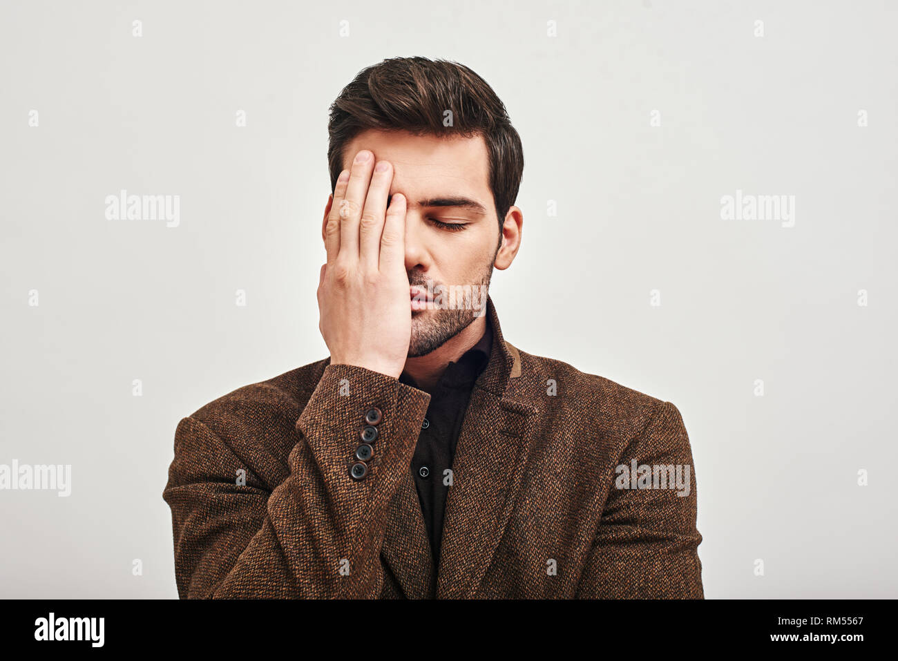 Portrait einer jungen gutaussehenden Mann, Braune Jacke, die seine Augen mit der Hand aufgrund von Müdigkeit auf weißem Hintergrund Stockfoto