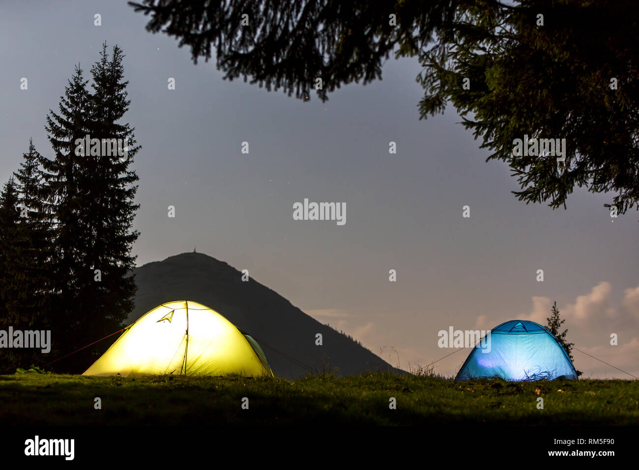 Zwei hell leuchtende, touristische Zelte auf der grünen Wiese Wald Lichtung auf dunklen Berg und dem klaren, blauen Sternenhimmel Kopie Raum Hintergrund. Tourismus, Nacht campin Stockfoto