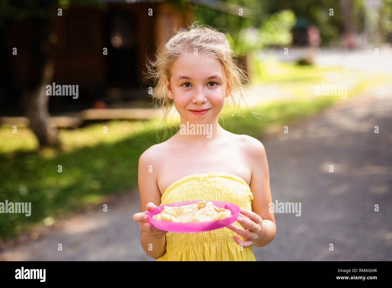 Blond lächelnde Mädchen mit Platte Pfannkuchen im Land. Stockfoto