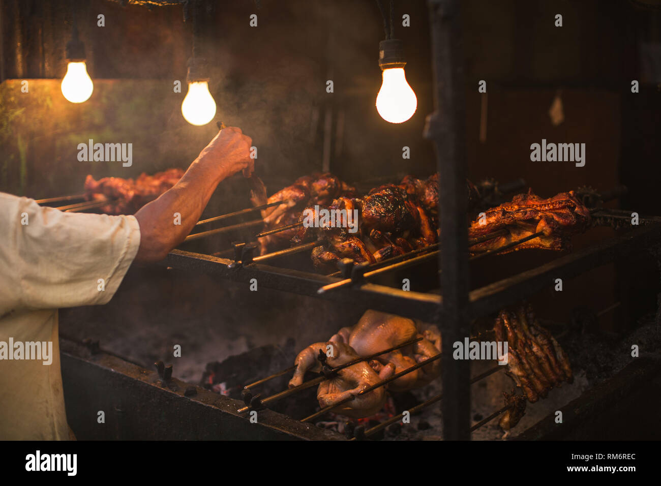 Outdoor street Chicken Grill mit Grill Spieß gebraten über dem Rauchen leben Kohlen in einem einfachen elektrischen Beleuchtung, die Philippinischen lechon Mann Stockfoto