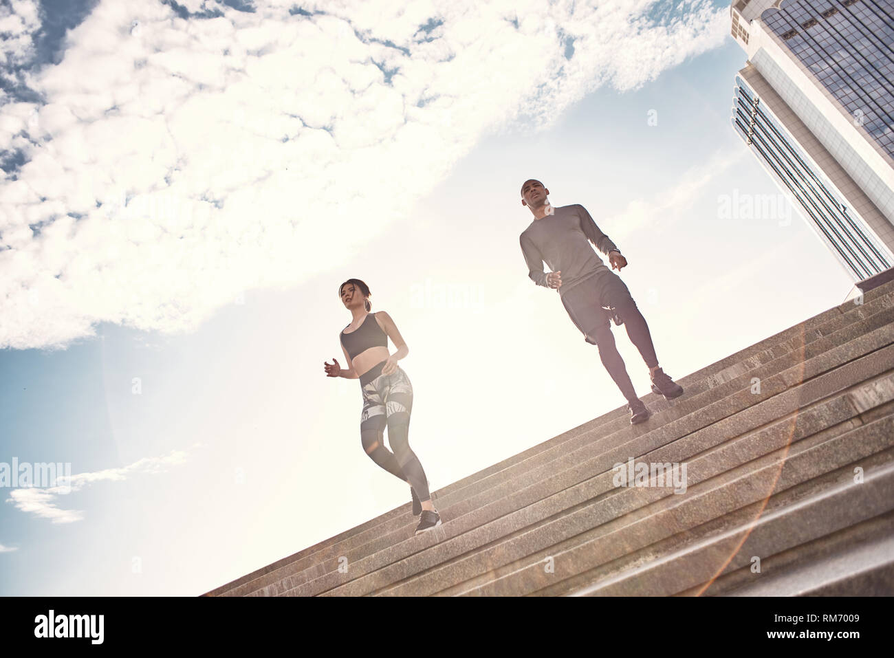 Aktiver Lebensstil. Schöne Frau und schöne schwarze Männer sind Joggen die Treppe hinunter, auf einer sonnigen warmen Tag. Gesunde Paare. Sport motivation Konzept. Fitness Concept. Frauen Schönheit. Gesundes Leben. Zusammen trainieren Stockfoto