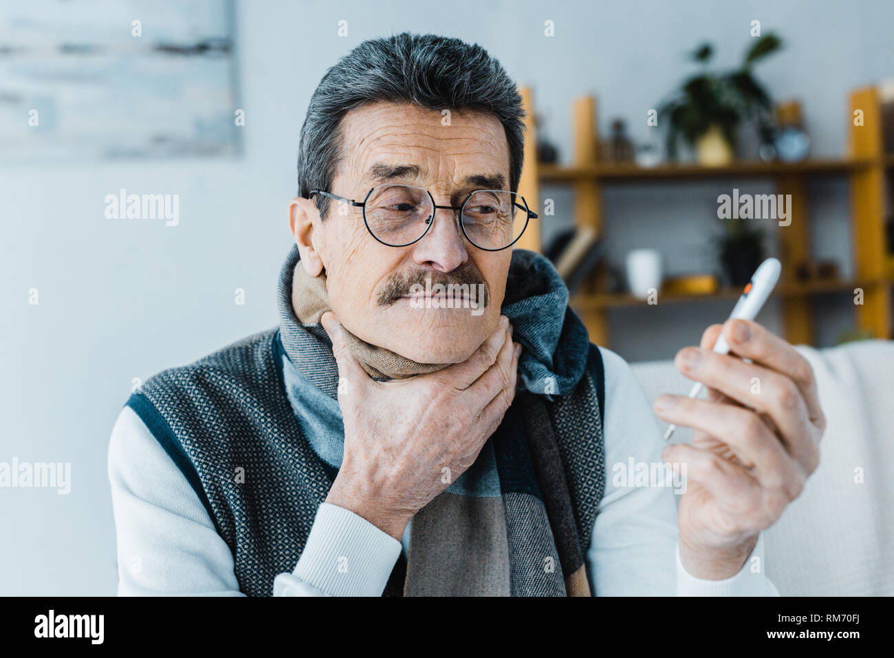 Kranken älteren Mann in Schal holding Kehle, während Sie Thermometer Stockfoto