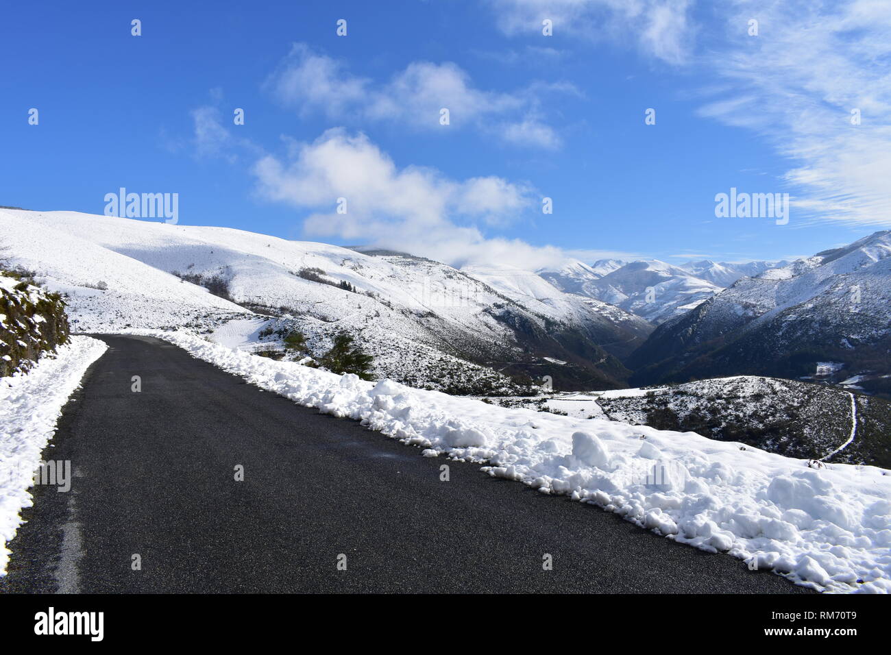 Winterlandschaft mit Straße und schneebedeckten Berge. Blauer Himmel mit Wolken. Ancares Region, Provinz Lugo, Galizien, Spanien. Stockfoto