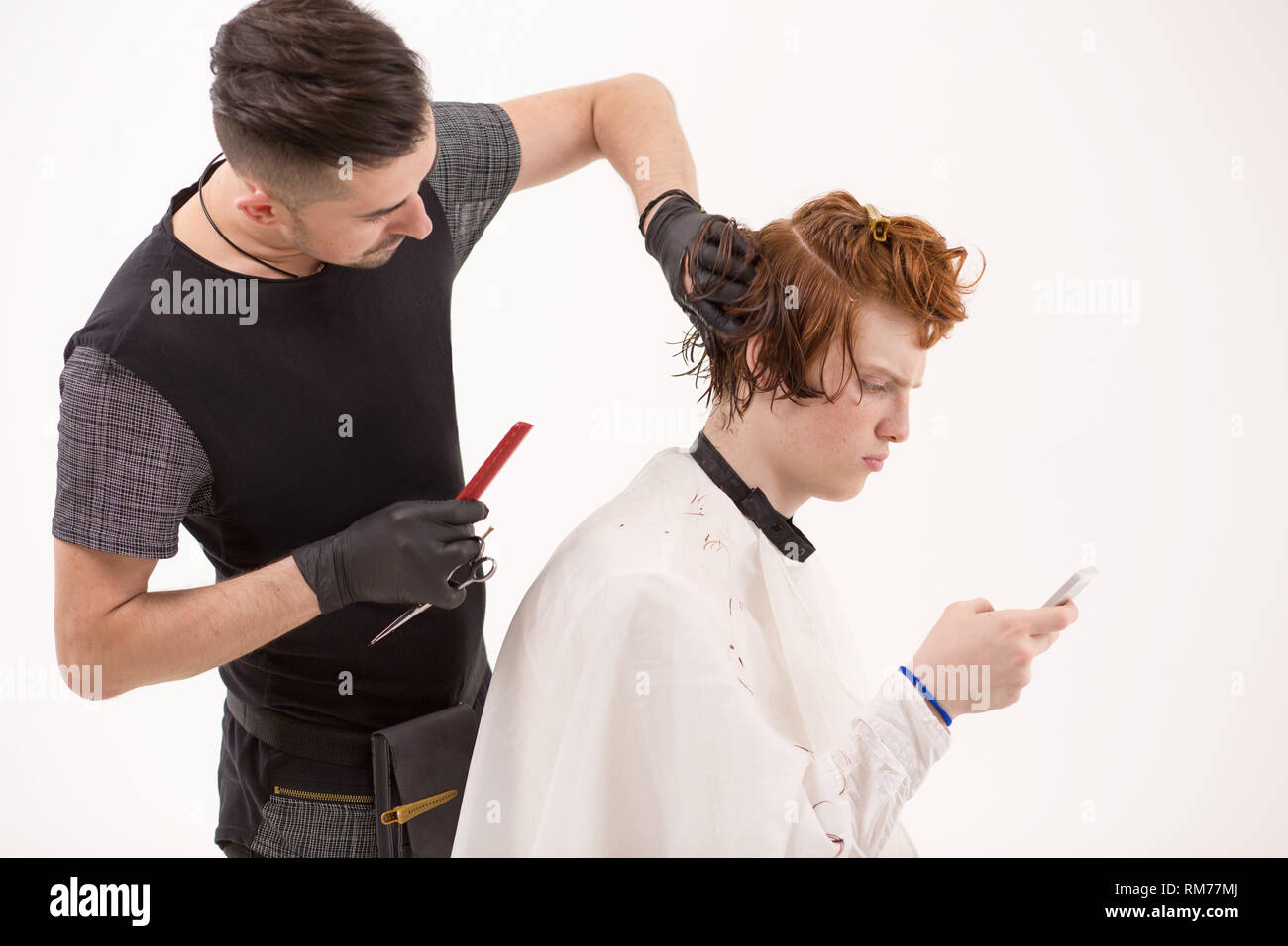 Stattliche Ingwer mann Browsen mit seinem Handy, während sich ein Haarschnitt Stockfoto