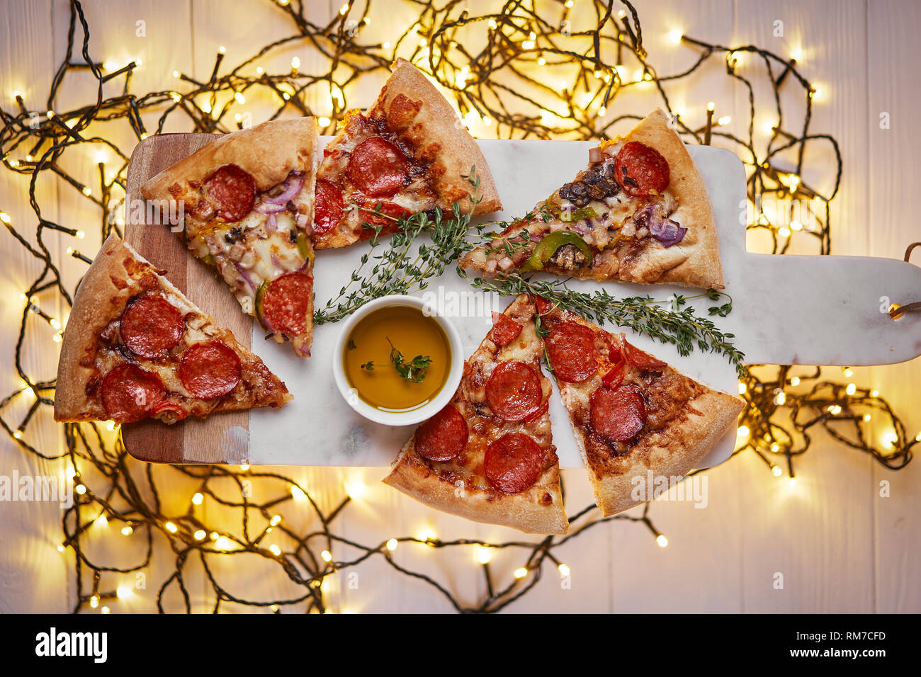 Weihnachten und Neujahr Atmosphäre. Heiße italienische Pizza mit Schmelzen mit Tomate, Salami und Käse auf einem weißen Marmor Schneidebrett. Hintergrund mit Beleuchtung Stockfoto