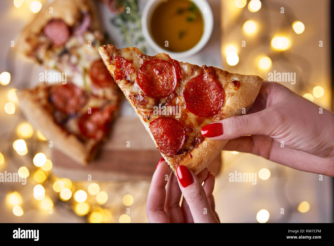 Weihnachten und Neujahr Atmosphäre. Womans hand nimmt Scheibe der Italienischen Pizza mit Schmelzen mit Tomate, Salami und Käse auf einem weißen Marmor Schneidebrett. Stockfoto
